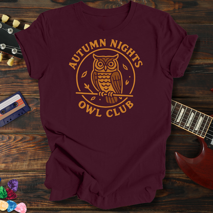 Maroon t-shirt with 'Autumn Nights Owl Club' design on a wooden surface with a guitar and cassette tape.