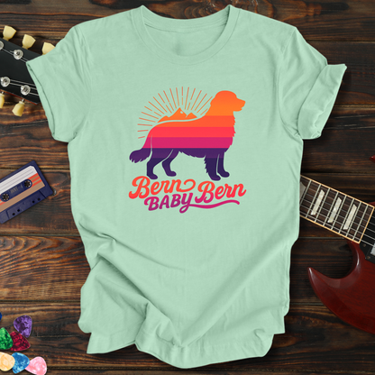 Light green t-shirt with a colorful dog graphic and text on a wooden surface with a guitar and cassette tape.