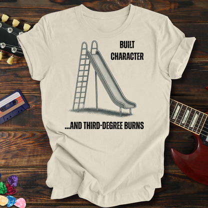 Beige t-shirt with graphic design and text on a wooden surface with a guitar and cassette tape.