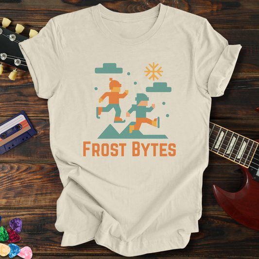 Beige t-shirt with 'Frost Bytes' graphic design on a wooden surface with a guitar and cassette tape.