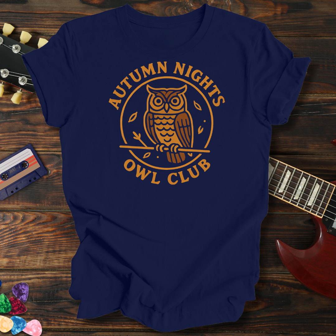Navy blue t-shirt with 'Autumn Nights Owl Club' design on a wooden surface with a guitar and cassette tape.