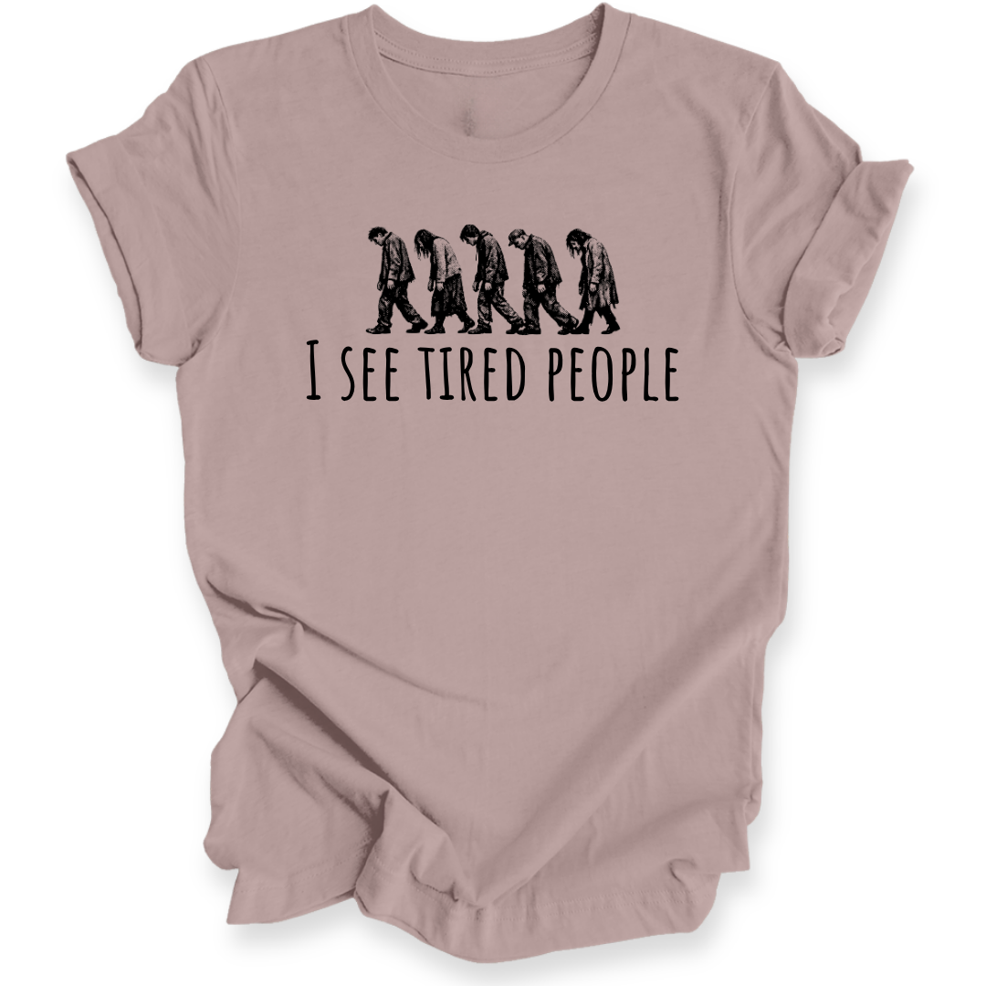 A dusty pink short-sleeve t-shirt with a black graphic of five progressively slacker-looking people walking side-by-side above the text 'I SEE TIRED PEOPLE'.
