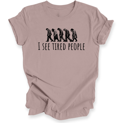 A dusty pink short-sleeve t-shirt with a black graphic of five progressively slacker-looking people walking side-by-side above the text 'I SEE TIRED PEOPLE'.