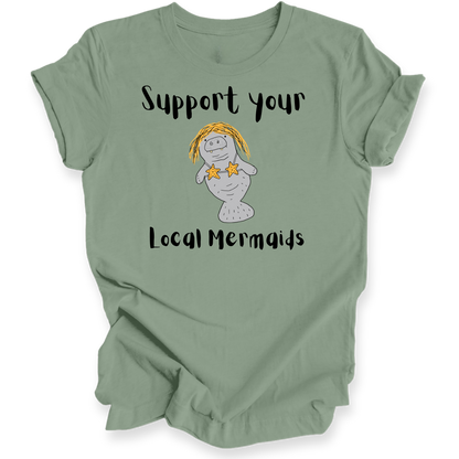 A sage green short-sleeve t-shirt with a graphic of a cartoon manatee wearing yellow hair and star earrings, with the text 'Support your Local Mermaids' printed in black.