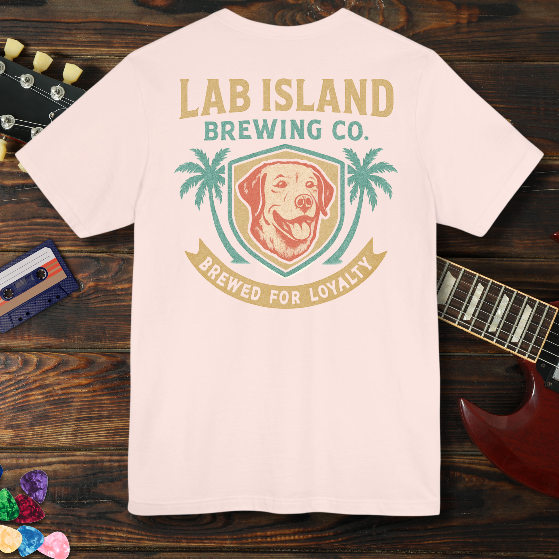 T-shirt with Lab Island Brewing Co. logo on a wooden surface with a guitar and cassette tape.