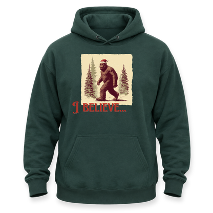 A dark green pullover hoodie with a front kangaroo pocket and a graphic print of Bigfoot wearing a Santa hat in a snowy forest, with the text 'I BELIEVE.