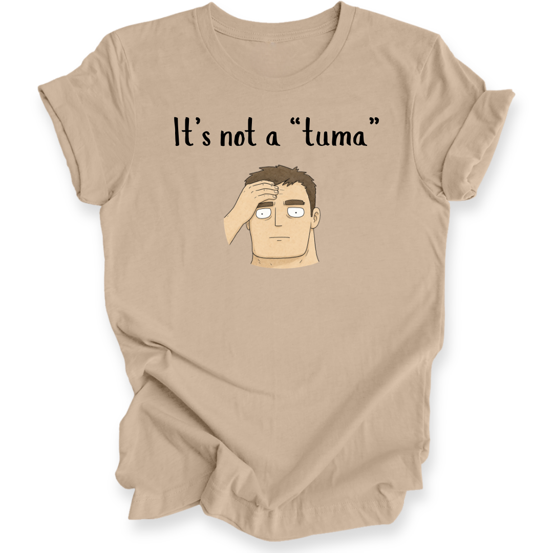 A tan short-sleeve t-shirt with a graphic print of a cartoon man's face and the text 'It's not a "tuma"' on the front, displayed against a plain white background.
