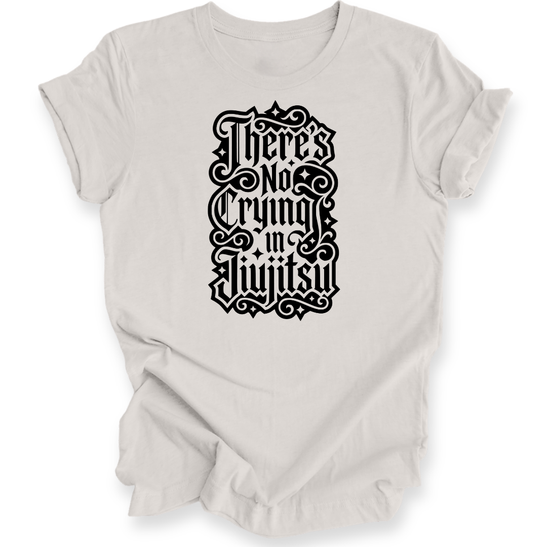 A light beige short-sleeve crewneck t-shirt with a black gothic-style graphic text print reading 'There's No Crying in JiuJitsu' on the front, displayed against a clean white background.