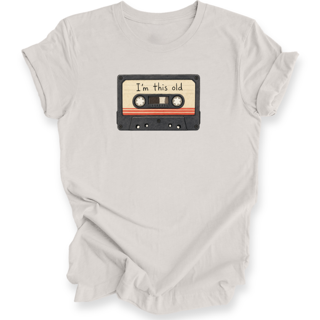 A light beige crewneck t-shirt with a graphic of a vintage cassette tape on the chest that reads 'I'm this old'.