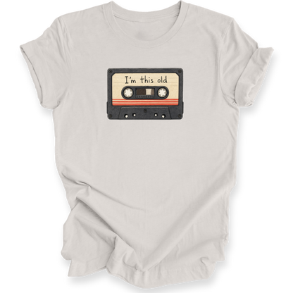 A light beige crewneck t-shirt with a graphic of a vintage cassette tape on the chest that reads 'I'm this old'.