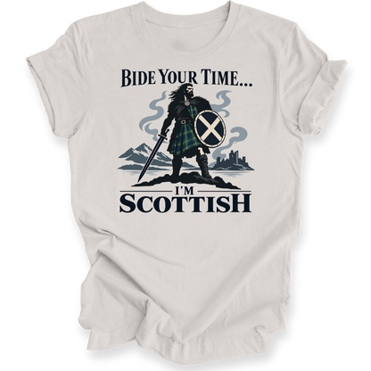 A light beige crewneck t-shirt with a graphic print of a Scottish warrior in a tartan kilt holding a sword and shield, with the text 'BIDE YOUR TIME.