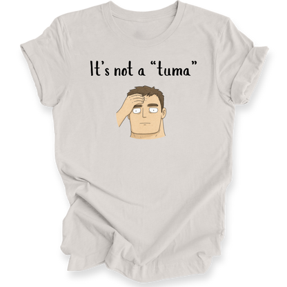 A light beige graphic t-shirt featuring the text 'It's not a "tuma"' above a cartoon illustration of a confused man with his hand on his head, displayed on a clean white background.
