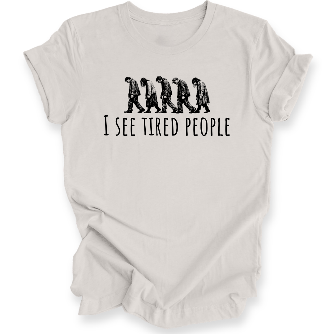 A light beige crewneck t-shirt with a black graphic of five progressively slouching figures and the text 'I SEE TIRED PEOPLE' printed on the chest, displayed against a solid white background.