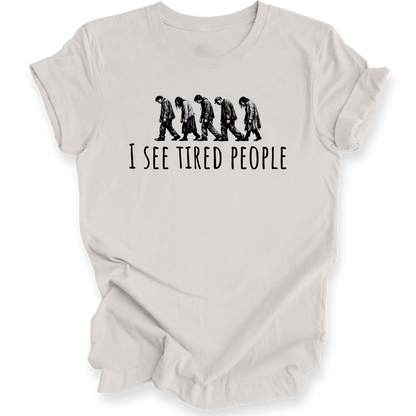 A light beige crewneck t-shirt with a black graphic of five progressively slouching figures and the text 'I SEE TIRED PEOPLE' printed on the chest, displayed against a solid white background.