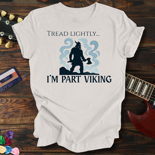 White t-shirt with 'Tread Lightly... I'm Part Viking' design on a wooden surface with a guitar and cassette tape.