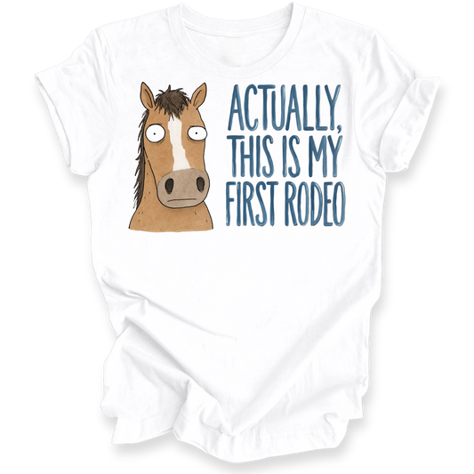 A white short-sleeve crewneck t-shirt featuring a graphic print of a brown cartoon horse and the text 'ACTUALLY, THIS IS MY FIRST RODEO' in blue lettering.