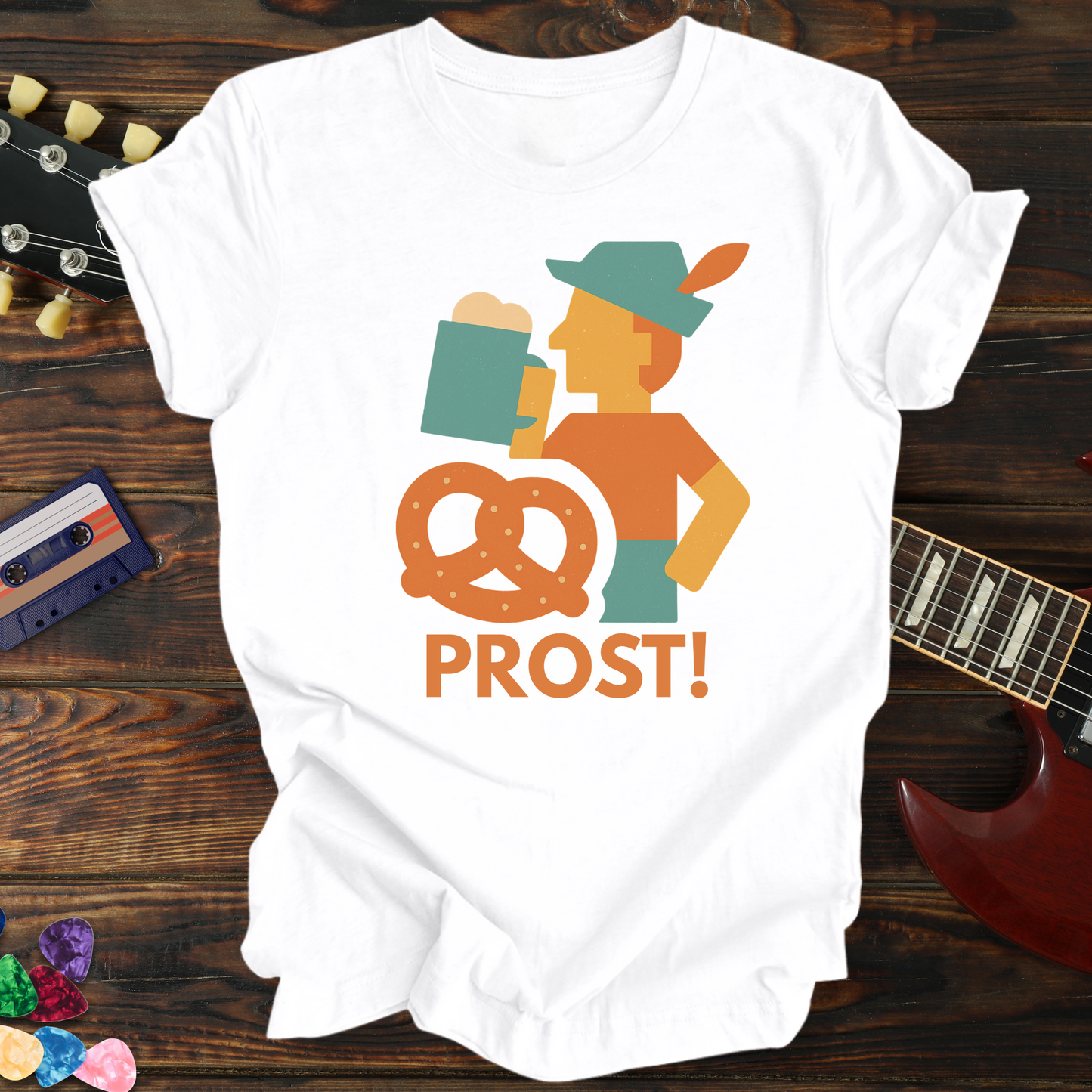 White t-shirt with 'PROST!' graphic design on a wooden surface with a guitar and cassette tape.