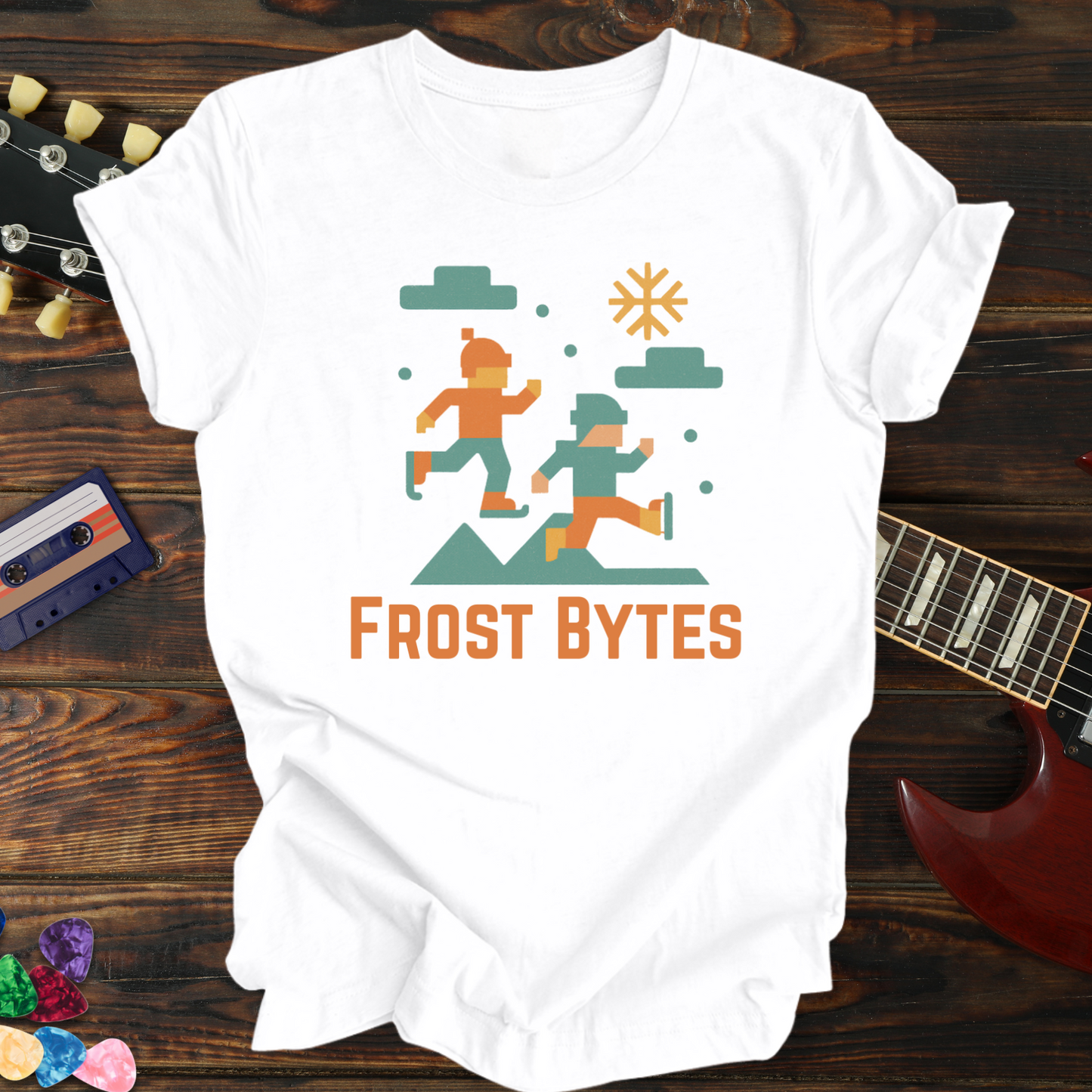 White t-shirt with 'Frost Bytes' graphic design on a wooden surface with a guitar and cassette tape.
