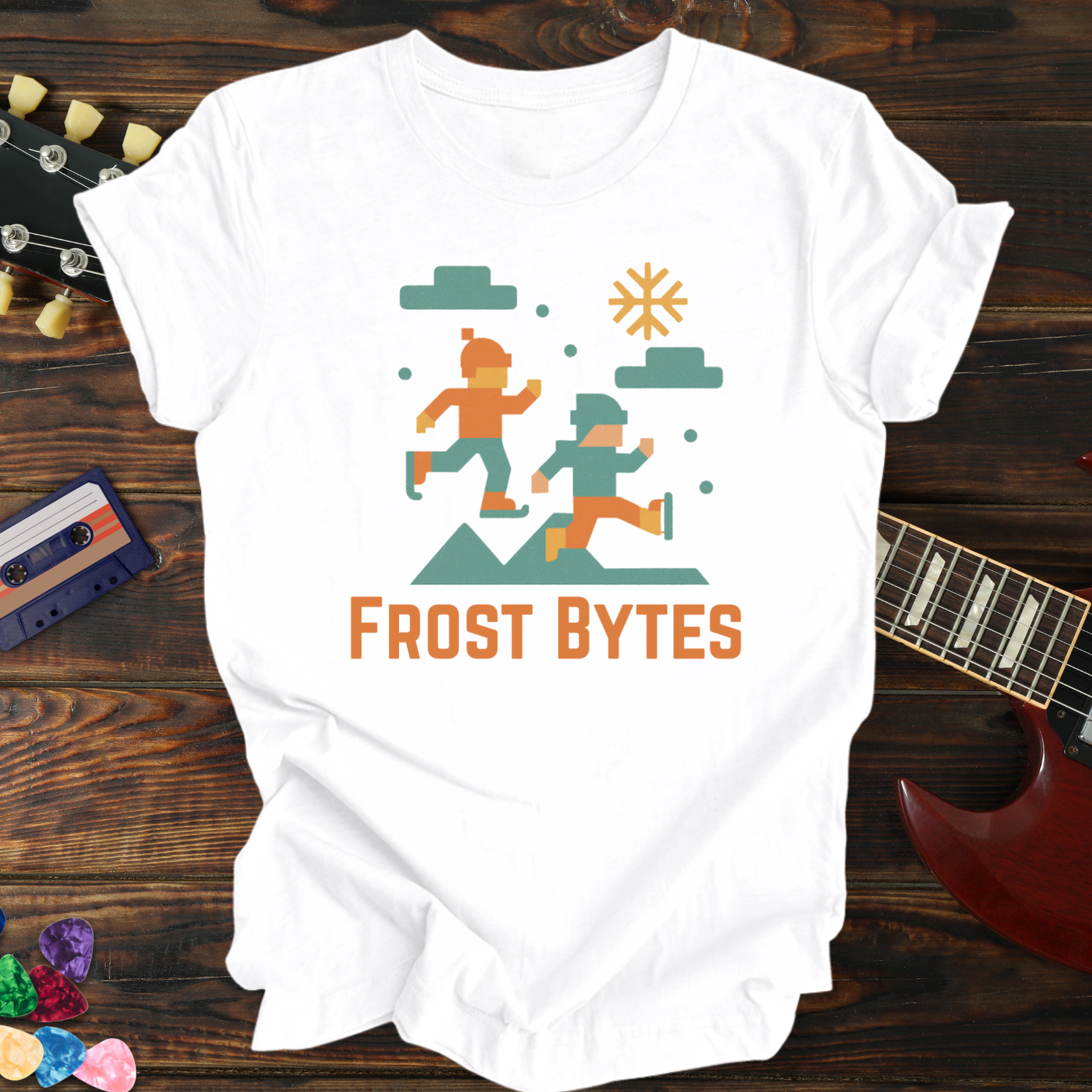 White t-shirt with 'Frost Bytes' graphic design on a wooden surface with a guitar and cassette tape.