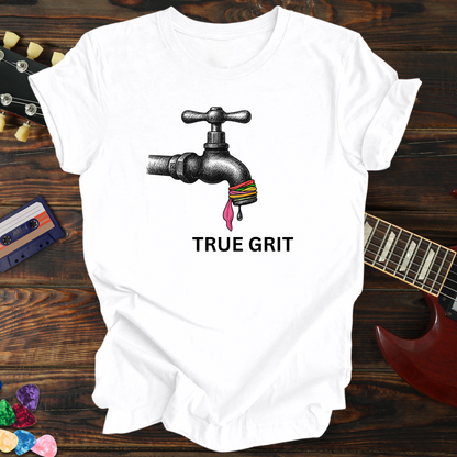 White t-shirt with a graphic of a faucet and colorful beads, text 'TRUE GRIT', on a wooden background with a guitar and cassette tape.