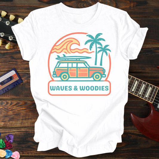 White t-shirt with 'Waves & Woodies' design on a wooden surface with a guitar and cassette tape.