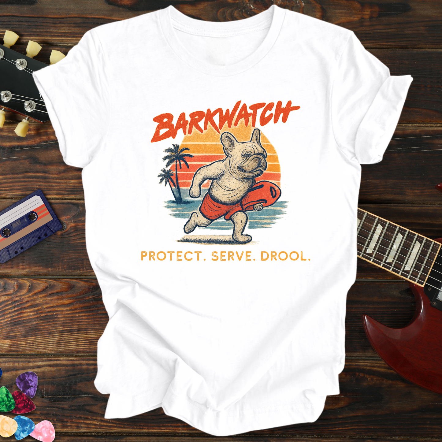 White t-shirt with 'Barkwatch' graphic on a wooden surface with a guitar and cassette tape.