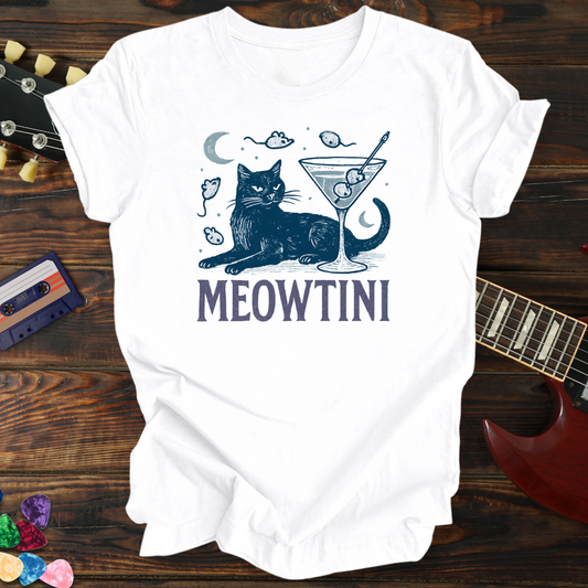 White t-shirt with a cat-themed graphic and 'MEOWTINI' text on a wooden surface with a guitar and cassette tape.