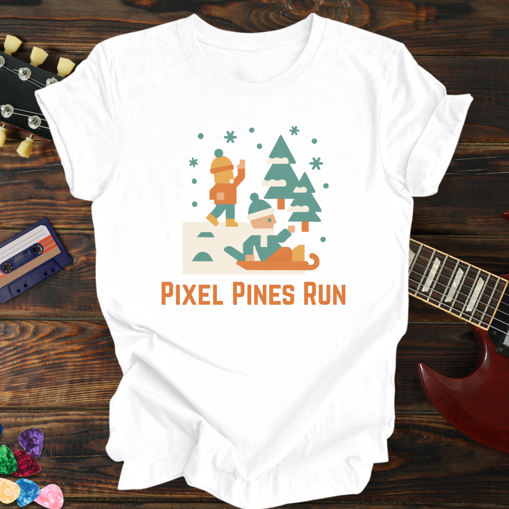 White t-shirt with 'Pixel Pines Run' graphic design on a wooden surface with a guitar and cassette tape.