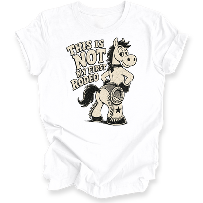 A white short-sleeve t-shirt with a graphic print of a cartoon horse wearing chaps and boots, next to the text 'THIS IS NOT MY FIRST RODEO'.