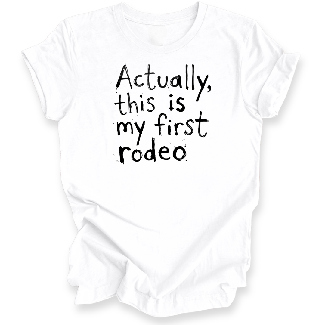 A white short-sleeve t-shirt with black hand-drawn text reading 'Actually, this is my first rodeo' on the front, displayed against a clean white background.